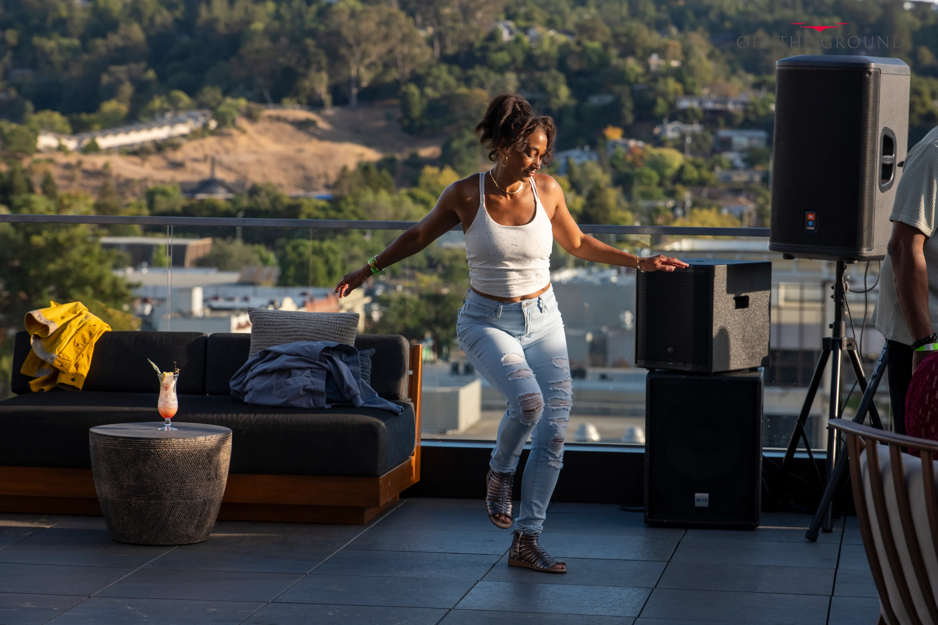 A woman dancing on the rooftop near the speakers with hills behind her